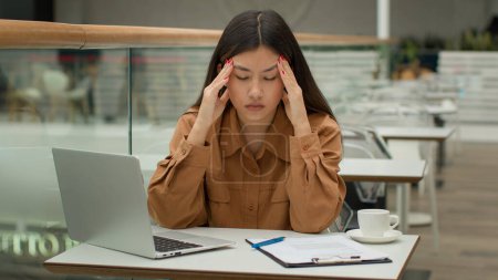 Téléchargez les photos : Stressé fatigué femme asiatique travaillant dans un café avec ordinateur portable problème de paperasserie difficulté d'affaires malade malsaine femme d'affaires coréenne chinoise a mal à la tête migraine souffrir mal tension surmenage - en image libre de droit