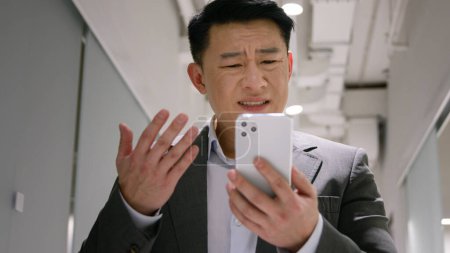 Foto de Frustrado molesto asiático de mediana edad hombre hombre chino empresario coreano empleador leer mal mensaje en el teléfono móvil preocupado colapso de la deuda quiebra fracaso ruptura teléfono inteligente shock problemas en la oficina - Imagen libre de derechos