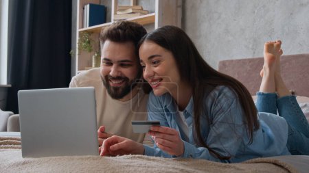 Kaukasisches Paar glücklich Frau und Mann Blick auf Laptop-Bildschirm auf dem Bett zu Hause aufgeregt lächelnd Frau und Mann zahlen Geld online verwenden Bankkreditkarte Familienbudget E-Commerce kaufen Waren einkaufen für Schlafzimmer
