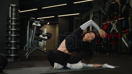 Téléchargez les photos : Fit mince sportive caucasienne athlétique femme active saine étirement des muscles du corps entraînement côté flexion exercice de flexion en position lotus entraîneur de fitness fille sportive étirement yoga sport séance d'entraînement à la salle de gym - en image libre de droit