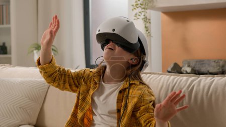 Photo for Funny caucasian kid girl child schoolgirl having fun in virtual reality headset at home couch playing online video game in world metaverse using innovative technology VR glasses exploring cyberspace - Royalty Free Image