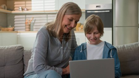 Photo for Caucasian elderly woman 50s with grandson browsing social media on laptop shopping in online store talking smiling laughing at home couch caring grandmother helping kid boy child studying on internet - Royalty Free Image