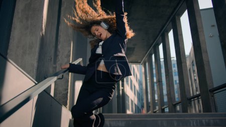 Photo for Joyful happy Caucasian young business woman girl worker dancing walking down on stairs outside carefree businesswoman have fun listen music in headphones dance sing in city sunlight celebrate achieve - Royalty Free Image