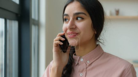 Téléchargez les photos : Arabe femme fille étudiant parler téléphone portable au bureau à la maison partage nouvelles parler téléphone portable femme propriétaire femme d'affaires parler smartphone communiquer avec un ami conversation d'appel en ligne raconter des commérages - en image libre de droit