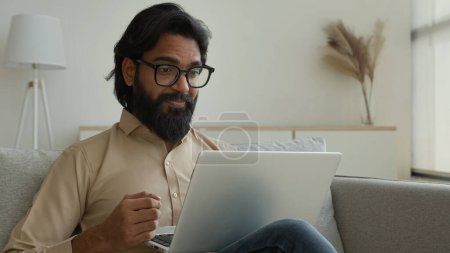 Photo for Arabian muslim man freelancer working from home focused millennial guy indian businessman typing on computer laptop surfing internet looking at screen sitting on couch distant remote job on quarantine - Royalty Free Image