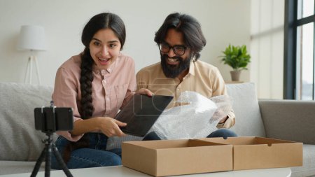 Photo for Couple bloggers customers open package box order online shopping delivery excited happy Arabian man and woman record blog stream on mobile phone at home open parcel win digital tablet unpacking video - Royalty Free Image