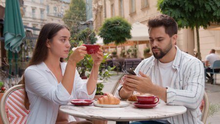Photo for Young frustrated disappointed woman upset offended drinking coffee city outside cafe Caucasian separated man busy mobile phone telephone lack of attention ignoring couple relationship problem breakup - Royalty Free Image
