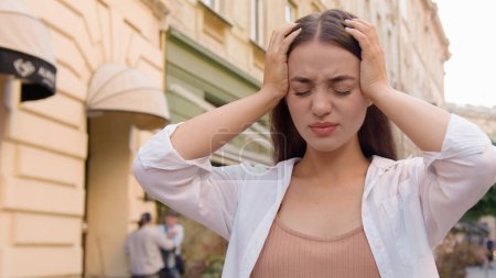 Photo for Young Caucasian unhappy woman holding head headache problem unhealthy tired female anxiety touching illness migraine painful suffering discomfort eyes closed disease symptom sick city outside street - Royalty Free Image