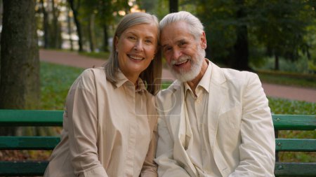 Téléchargez les photos : Portrait mignon romantique heureux aînés famille souriant caucasien vieux couple homme femme câlins discuter regarder caméra repos ensemble en dehors de la ville parc santé retraite mariage - en image libre de droit