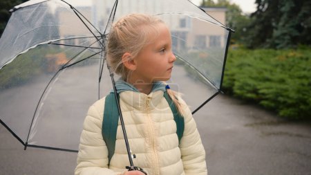 Photo for Little European girl looking at camera smiling holding umbrella rainy weather child pupil kid city outside park expression funny childish parasol backpack primary school kindergarten preschool enjoy - Royalty Free Image