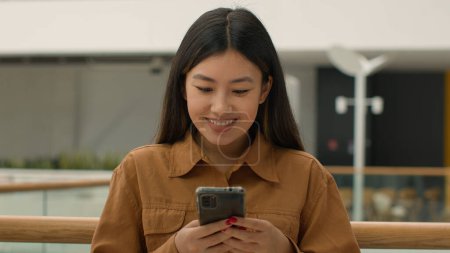 Téléchargez les photos : Gros plan souriant asiatique chinois japonais femme portrait multiracial fille femme d'affaires lire les médias sociaux smartphone écran utiliser téléphone portable dans le bureau coréen ethnique femme étudiante chat message - en image libre de droit