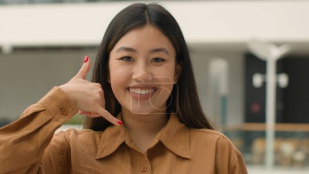 Téléchargez les photos : Gros plan femme asiatique heureux souriant japonais coréen fille femme d'affaires regardant à la caméra faisant geste de téléphone hey vous me rappeler conversation proposition d'appeler numéro de téléphone portable - en image libre de droit