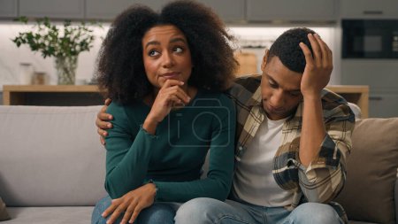 Photo for Annoyed African American ethnic exhausted young couple disturbed parents sitting sofa thinking feeling tired about noisy little boy hyperactive child misbehaving kid son playing run inside living room - Royalty Free Image