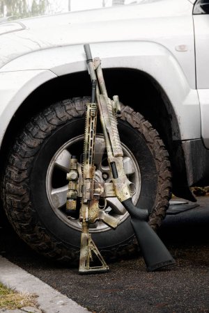 Photo for A shotgun and a rifle gun standing against the wheel of a silver SUV - Royalty Free Image
