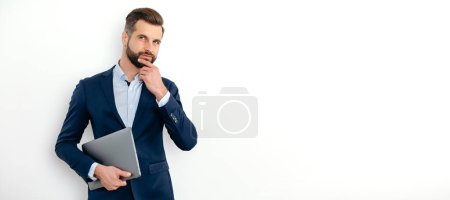 Panoramic photo of successful caucasian businessman, seo, executive, broker, financial adviser, stand on isolated white background, holding laptop, looking to the side, thinking over idea. Copy-space