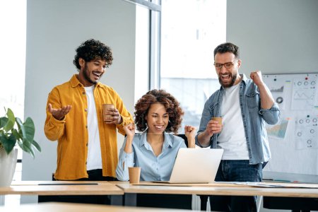Téléchargez les photos : Groupe joyeux de gens d'affaires multiraciaux motivés et prospères, travaillant ensemble sur un projet dans un bureau moderne, utilisant un ordinateur portable, discutant d'idées, réfléchissant, se réjouissant du succès, souriant - en image libre de droit