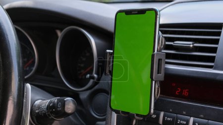 Téléchargez les photos : Smartphone or GPS, navigator device in a holder in car with blur background of traffic jams in the evening. Mockup green empty screen for text, copy space. High quality photo - en image libre de droit