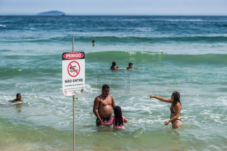 Téléchargez les photos : Rio de Janeiro, Brésil - Janvier 3, 2024 : Les gens nagent à Copacabana Beach malgré un signe en portugais avertissement de ne pas en raison de forts courants - en image libre de droit