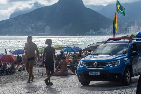 Foto de Río de Janeiro, Brasil - 29 de enero de 2024: Un coche de la policía brasileña atraviesa la bulliciosa playa de Ipanema en Río de Janeiro, rodeado de lugareños que buscan el sol y turistas disfrutando del clima agradable - Imagen libre de derechos