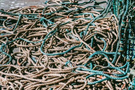 An assortment of brown and green fishing nets and ropes lay entangled on a concrete dock, illuminated by the bright daylight, suggesting recent maritime activity in a bustling fishing area