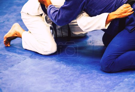 Two men on a blue mat in a Brazilian Jiu-Jitsu training facility. He is focused and practicing the techniques of the martial art.