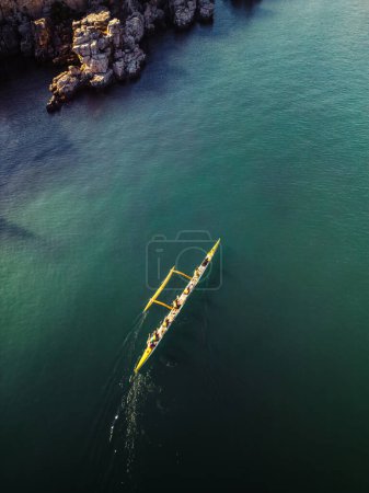 Perspectiva aérea captura una canoa amarilla remada por un grupo de personas que navegan por las tranquilas aguas azules cerca de una costa rocosa durante el día