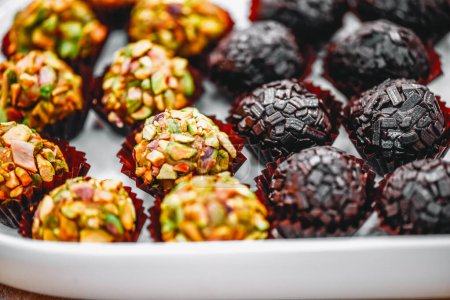 A delightful assortment of Brigadeiro is presented on a serving tray, featuring two varieties - one with chocolate sprinkles and another with a pistachio coatings.