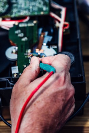 Ein Techniker repariert am Nachmittag in einer Werkstatt eine Platine eines elektronischen Geräts. Seine Hände sind mit Werkzeugen zu sehen, um Bauteile auf der Leiterplatte zu fixieren.