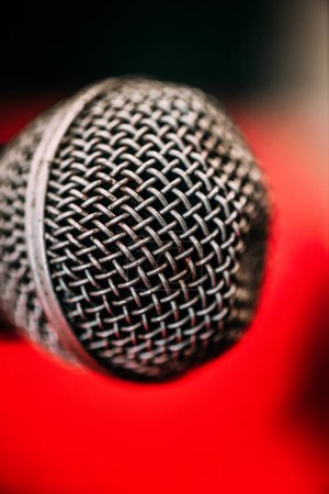 A detailed macro shot showcasing a microphones intricate wire mesh and texture, set against a vibrant red backdrop, highlighting the energy of an evening concert performance.