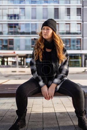 Photo for Woman in her mid-thirties with long red hair wearing a cap and black clothing in an urban location. - Royalty Free Image