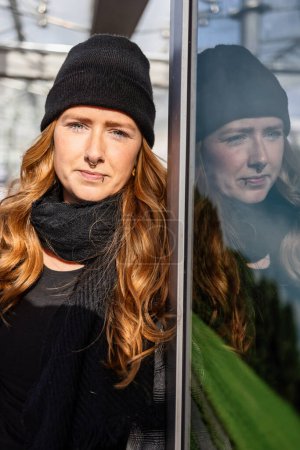 Photo for Woman in her mid-thirties with long red hair wearing a cap and black clothing in an urban location. - Royalty Free Image