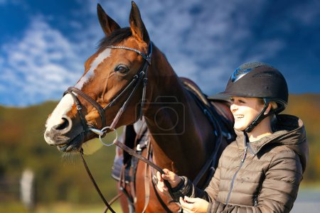 Photo for A portrait shot of a horse's head against a blue sky, the rider stands next to the horse. A sunny autumn day in nature. - Royalty Free Image
