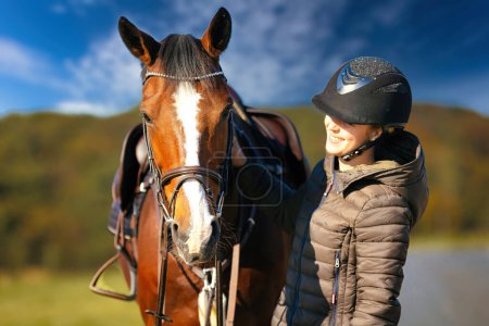 Photo for A portrait shot of a horse's head against a blue sky, the rider stands next to the horse. A sunny autumn day in nature. - Royalty Free Image