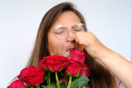 Photo for Bouquet of flowers, red roses, unhappy middle-aged woman 50 years old with bulging eyes from bewilderment and surprise, dissatisfaction with gift, flower pollen allergy, emotional female portrait - Royalty Free Image