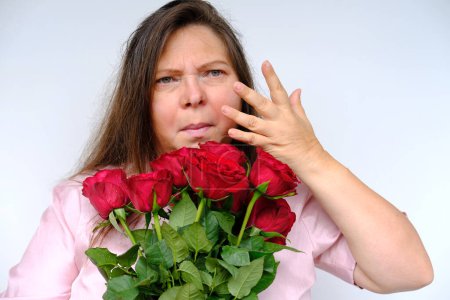 Photo for Bouquet of flowers, red roses, middle-aged woman 50 years old with allergies with bulging eyes from bewilderment and surprise, flower pollen allergy, close-up emotional female portrait - Royalty Free Image