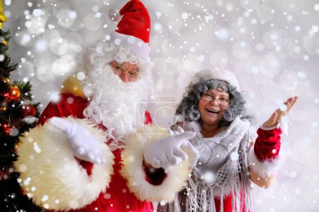 Téléchargez les photos : Vieux père Noël claus avec sa femme félicite les enfants et les adultes, montre avec les mains, concept de Noël, enfance, humeur festive, félicitations, bons voeux - en image libre de droit