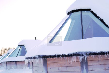 Foto de Pueblo cubierto de nieve, granja de ciervos Lapinkyla en el soleado día de invierno, Laponia, norte de Finlandia, casas rurales con techo de cristal, cubierto de nieve, tradicionalmente turismo, safari con el polo norte ártico finlandés - Imagen libre de derechos