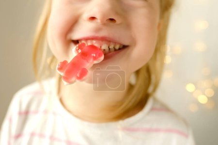 Téléchargez les photos : Portrait of small child, blonde girl 3 years old wants to eat gelatinous sweets, gummy bear, kid has a good appetite, happy childhood, balanced diet, sweet life, unhealthy food, halal food - en image libre de droit