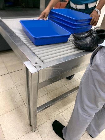 Photo for Passenger put his shoes on conveyor, airport security personnel takes plastic containers for gadgets, bags, boxes on way to X-ray machine airport checkpoint, air travel security requirement - Royalty Free Image