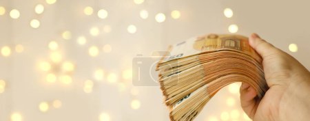 Téléchargez les photos : Female hand hold cash 50 euro banknotes on beautiful blurred creamy background with bokeh, payments to fund, gift for holiday, social assistance to poor, save up for vacation, car, winnings in casino - en image libre de droit