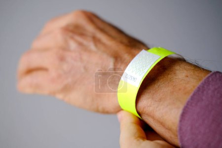 Photo for Close-up of neon yellow paper bracelet on the male arm of adult clinic patient, check tape with entry number on hand of middle-aged european man, event ticket concept - Royalty Free Image