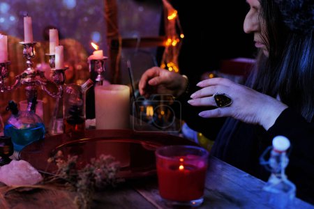 Téléchargez les photos : Session spiritualiste dans le salon de devin, sorcières, herboristes, diseuse de bonne aventure, les mains de milieu féminin faire des passages magiques sur plat rouge d'eau, brûler des bougies, sorts, rituels magie noire - en image libre de droit