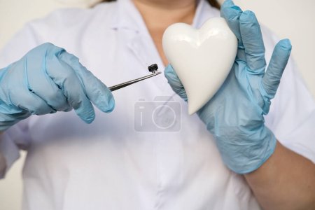 female scientist, doctor holding heart model, microprocessor, microchip, biochip tweezers for immunocytochemical studies heart, treatment cardiovascular disease, experimental nanotechnology medicine