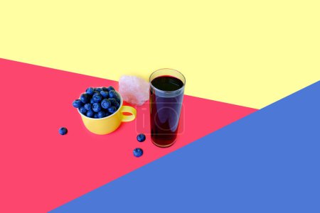 Vaccnium uliginosum, blue blueberries in yellow mug, glass of fresh juice, yellow and pink background, plant of Heather family, concept of healthy eating, vegan diet, raw food, healthy food