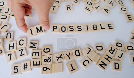 Photo for Close-up female hand holds square wooden alphabet blocks, word impossible turns into word possible on white background, self-identification, concept self-motivation and happiness, creative meaning - Royalty Free Image