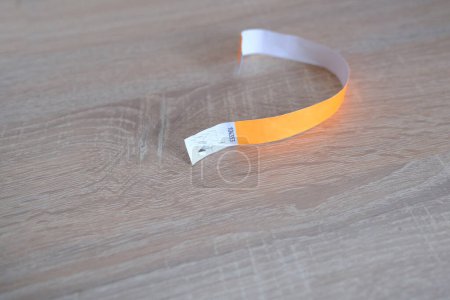 Photo for Close-up of yellow paper bracelet, check tape with entry number on wooden table, event ticket concept - Royalty Free Image