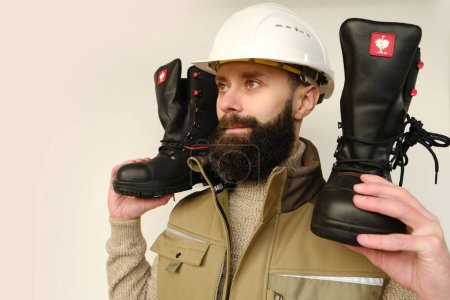 Photo for Pair black work Strauss boots made leather with reinforced cape, high top in hands of young bearded man, builder in uniform, highest product quality, professional workwear, Frankfurt- November 2022 - Royalty Free Image