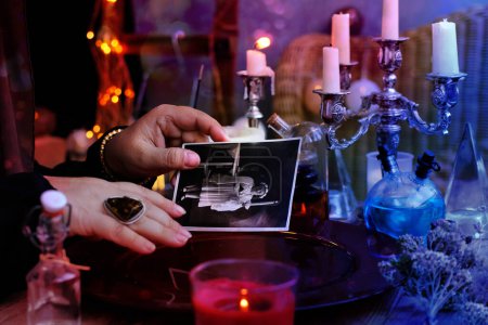 Photo for Spiritualistic seance in salon of medium with old photographs of deceased relatives, Female Fortuneteller or esoteric Oracle, longing for ancestors, communication with world spirits, help of ancestors - Royalty Free Image