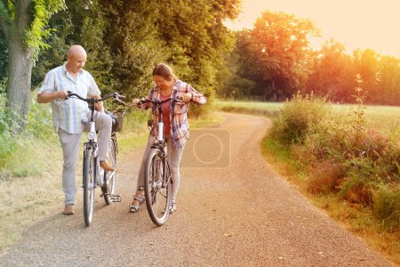 Téléchargez les photos : Personnes âgées, homme et femme mûrs avec des vélos, couples heureux promenades ensemble dans le parc, tour à vélo des beautés naturelles, moments précieux de la vie - en image libre de droit