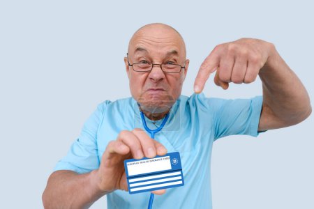 Photo for Mad doctor holds electronic public health insurance cheaper, Insurance Card, elderly physician with an expressive facial expressions aggressively shows European health insurance card, healthcare cost - Royalty Free Image